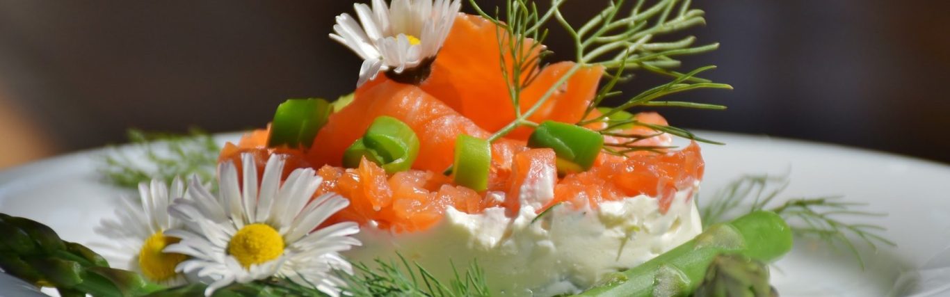 auf einem weißen Teller ist eine Lachsterrine angerichtet mit Kräutern, grünem Spargel und essbaren Blüten