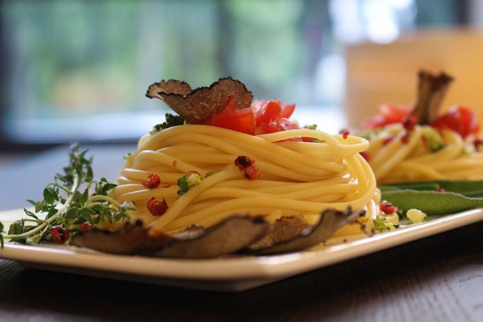 Spaghetti sind mit der Gabel zu kleinen Bergen gedreht. Oben auf dekoriert mit Trüffelscheibe, Tomatenstückchen und italienischen Kräutern