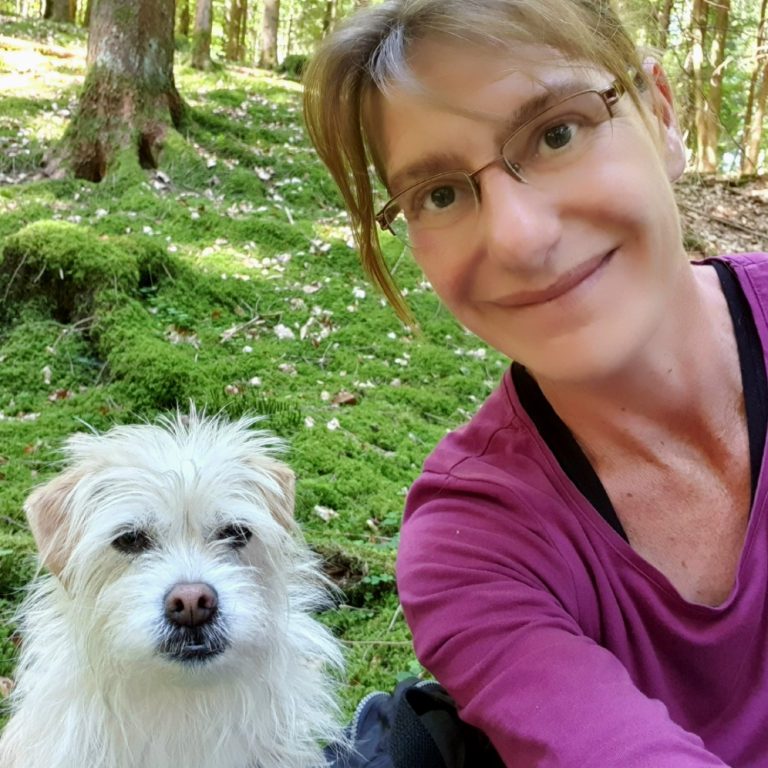 Unternehmerin Sabine Hörnicke und ihr kleiner weißer Hund Milly sind im grünen Wald